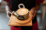 Barista serveert cappuccino met latte art bij blog over koffieproefpakketten