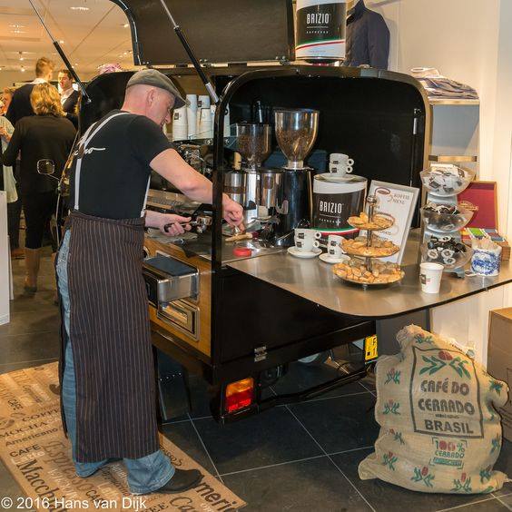 Barista aan het werk bij een mobiele espressobar met Brizio-koffie, omringd door verse bonen en zoetigheden.







