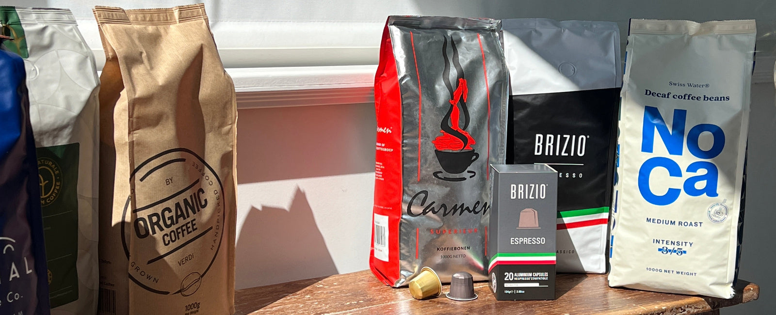 Assortiment koffieverpakkingen van GerritsKoffie met Carmen, Brizio, NoCa en Organic Coffee in zonlicht op een houten tafel.